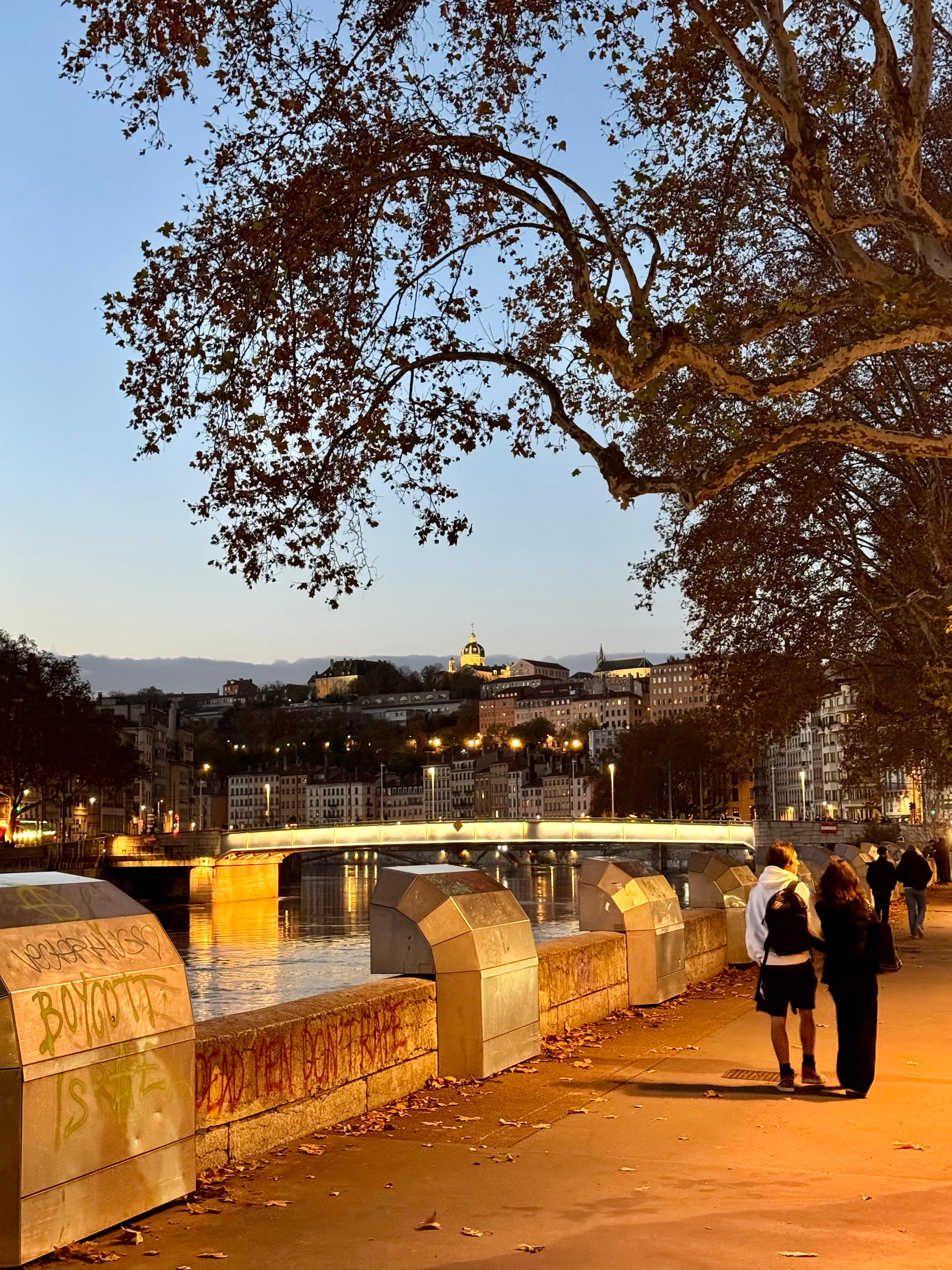 Couple walking along the Rhone riverbank at golden hour in Lyon