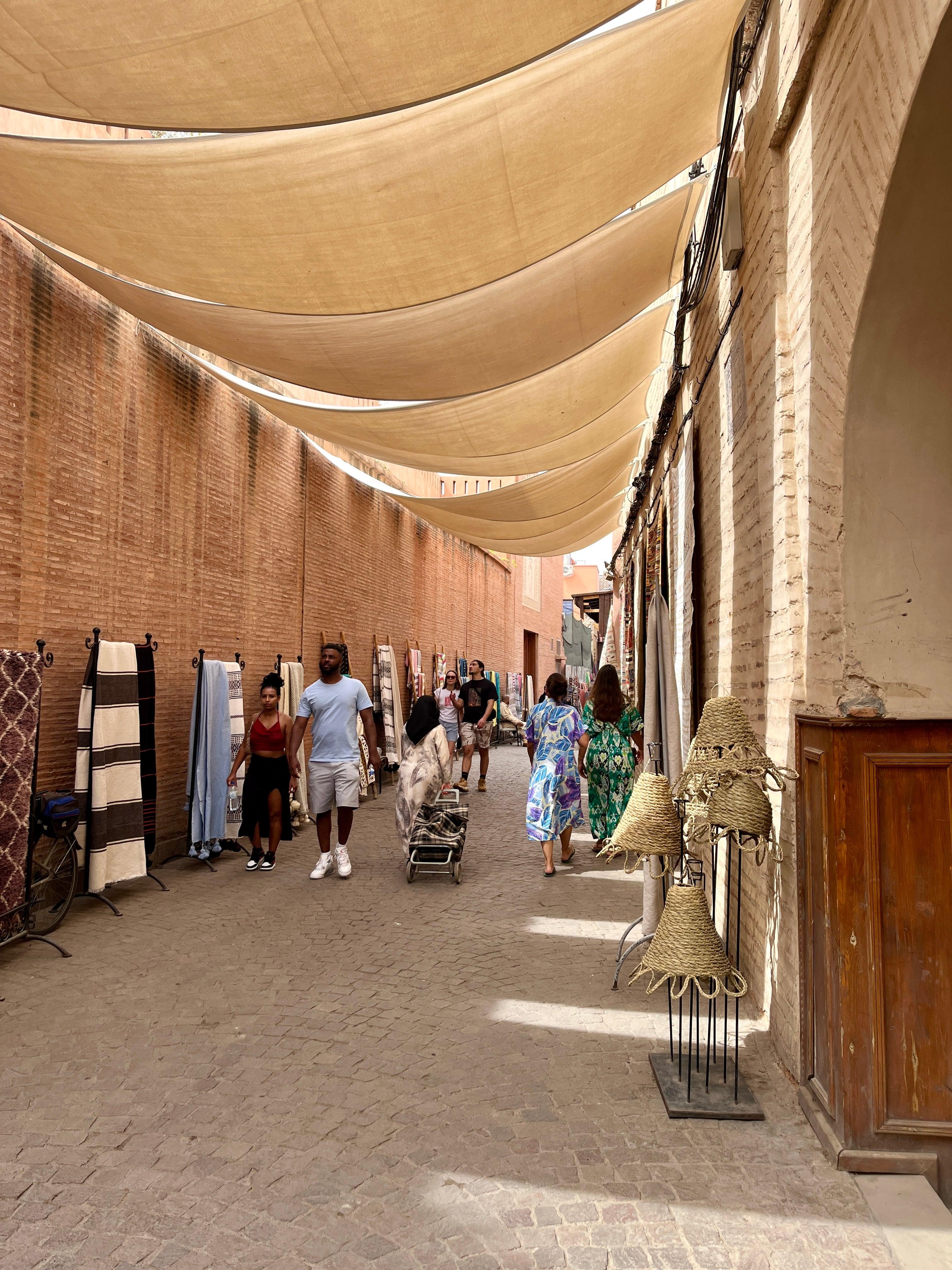 Sun-shaded alley with rugs and woven lamps in Marrakech medina