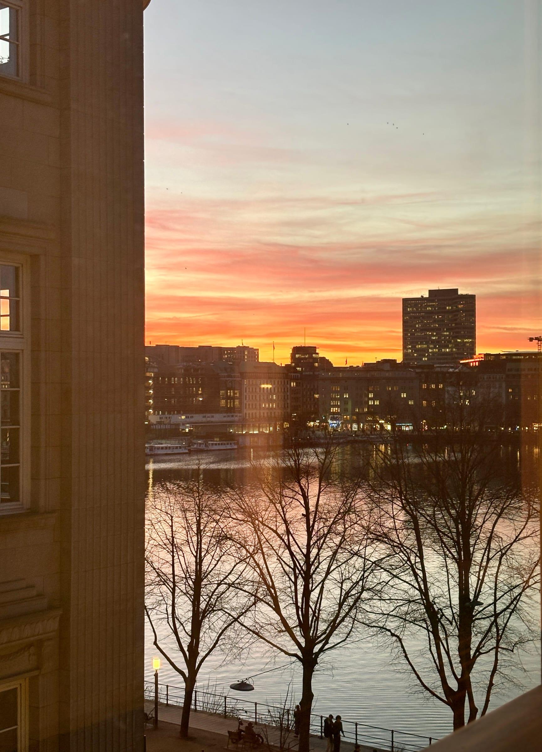 Sunset over the Alster lake in Hamburg with silhouetted trees and city skyline